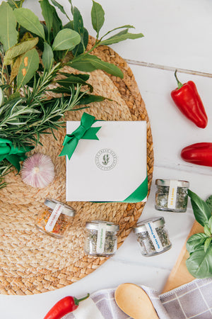 A White Card square box adorned with an elegant emerald green bow, proudly presented by The Fresh Herb Salt Company. Inside, the box holds four 20g glass pots of fresh herb sea salt seasoning, featuring flavors such as Original Italian, Chilli Garlic & Parsley, Herbes de Provence, and Dill Lemon and Garlic. A perfect and unique gift option that is both sustainable and eco-friendly, reflecting the company's commitment to quality and environmental consciousness.