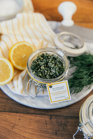 Delight your senses with this visually appealing scene featuring a glass Kilner jar filled with the vibrant flavors of Dill, Garlic, and Lemon Fresh Herb Seasoning blended into pure white coarse and fine sea salt. The jar's reusable design invites eco-conscious customers to refill with our practical pouches